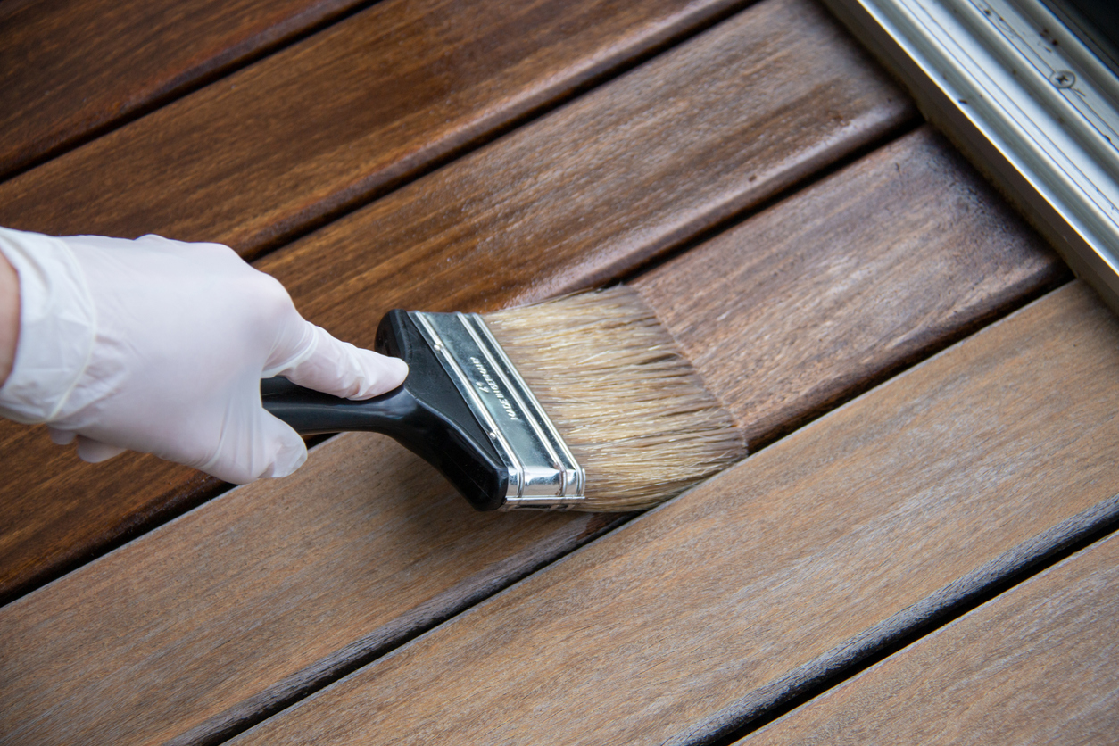 A paint brush staining a deck