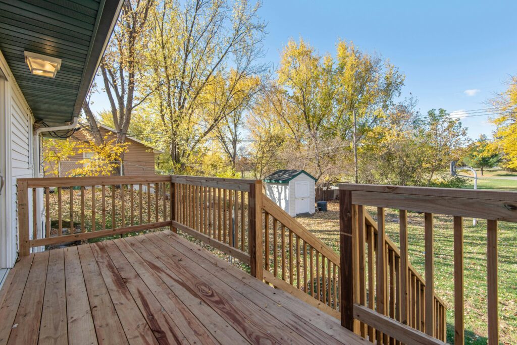 A stained deck leading down to a green backyard